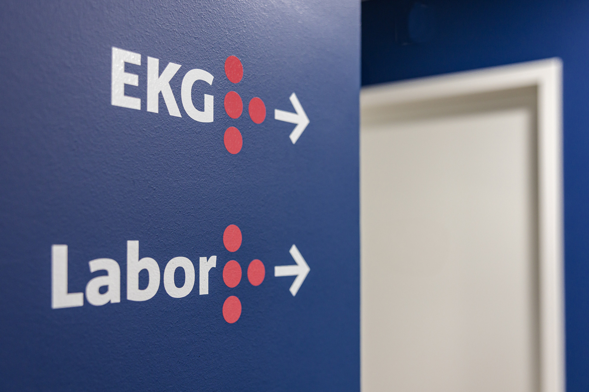 Orientierungssystem innerhalb der Praxisräume. die Beschriftungs an der blauen Wand zeigt den Weg zu den Räumen des EKG und des Labors.